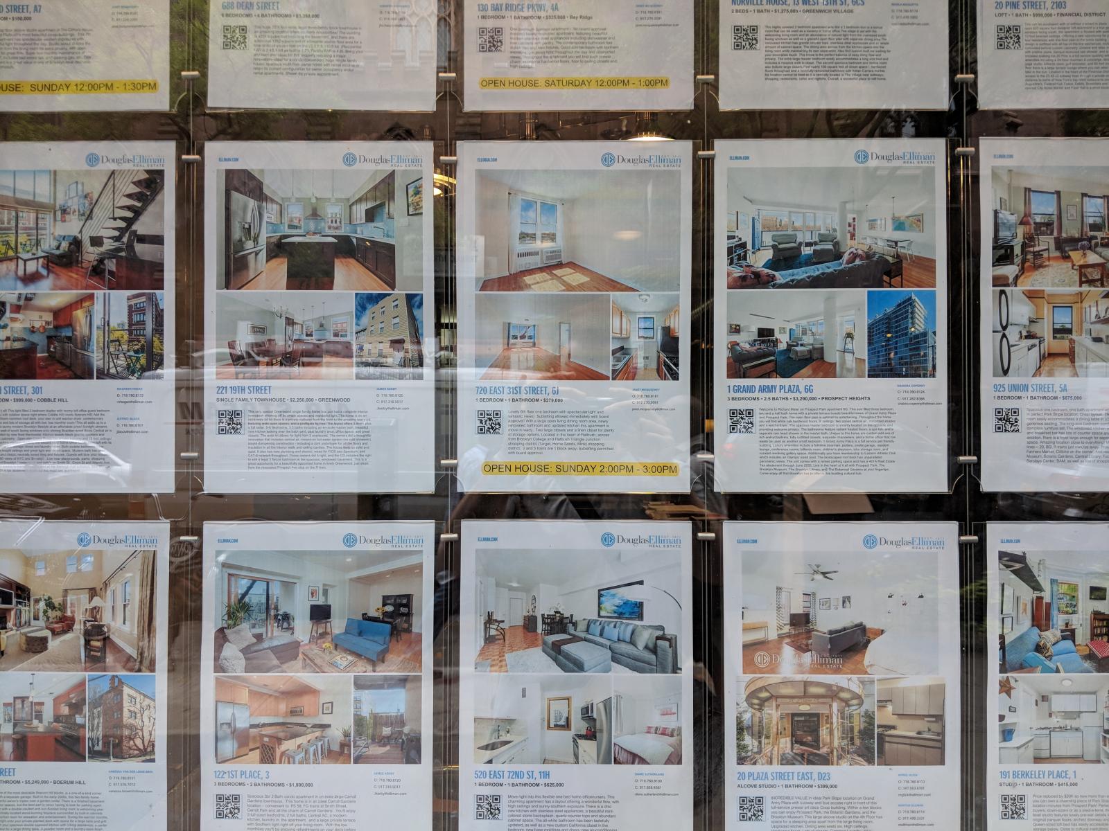 fifteen apartment posters in real estate office window, each displaying a photo of the apartment with the price and relevant apartment information.